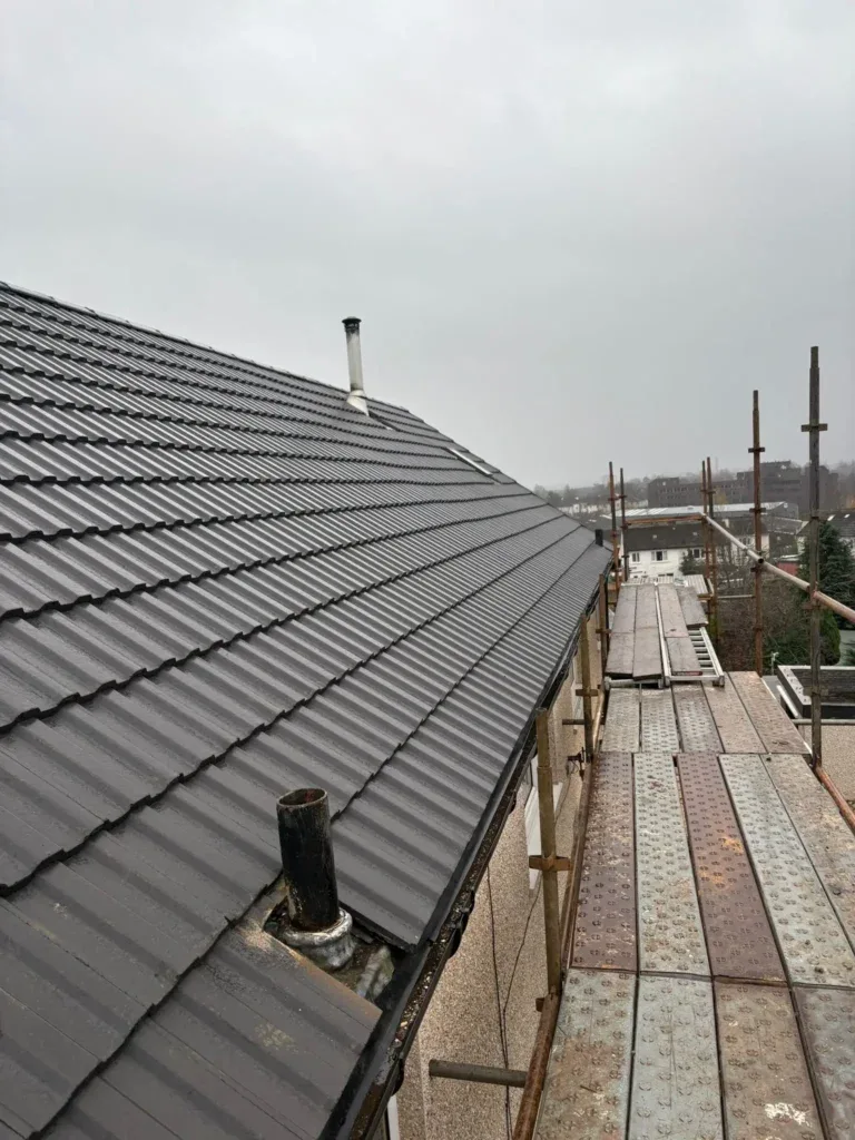 Newly completed dark grey tiled roof with scaffold access at the eaves