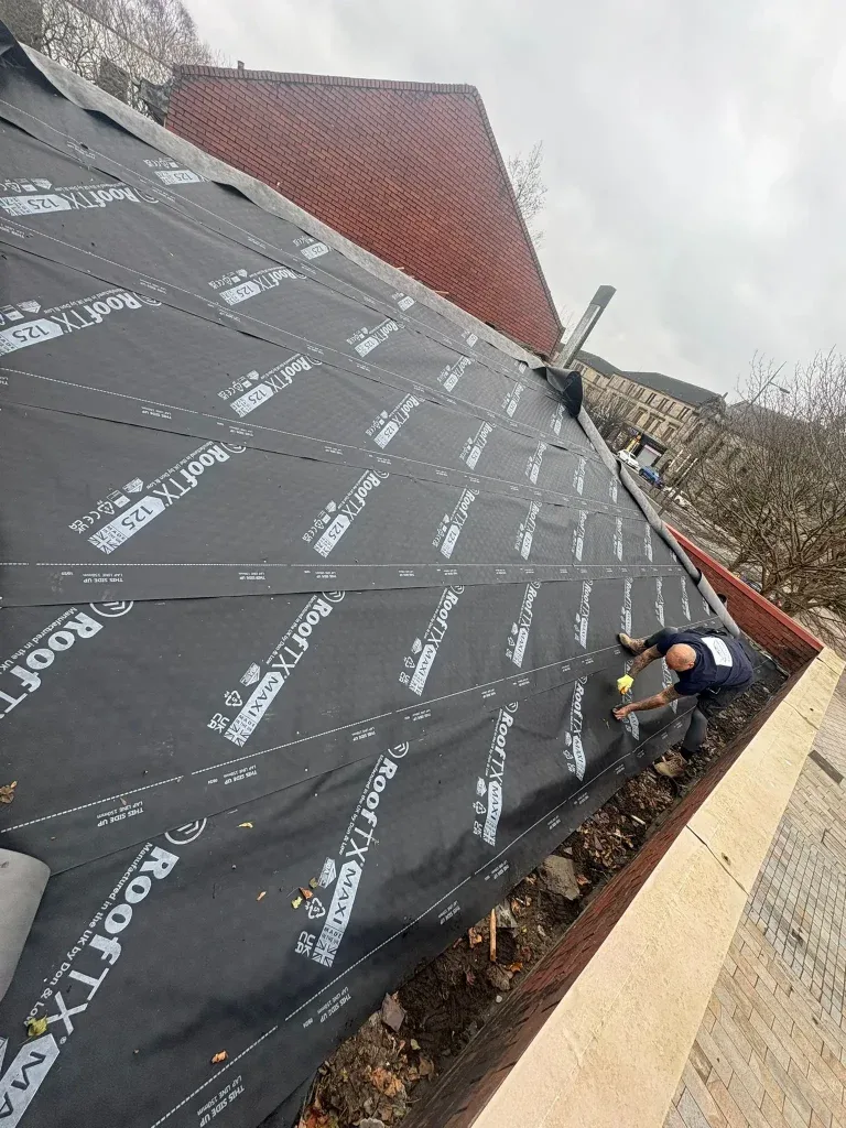 Roofer installing waterproof roofing underlay membrane ahead of tiling